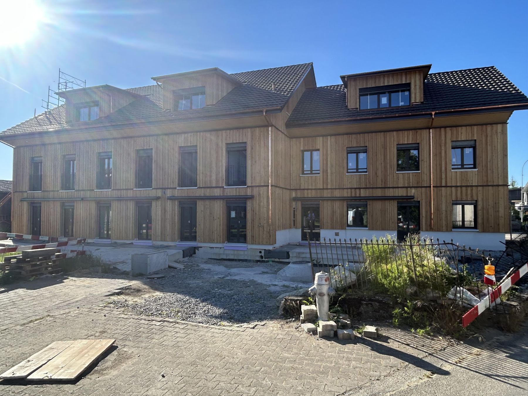 Mehrfamilienhaus mit Holzfassade, im Vordergrund die Baustelle